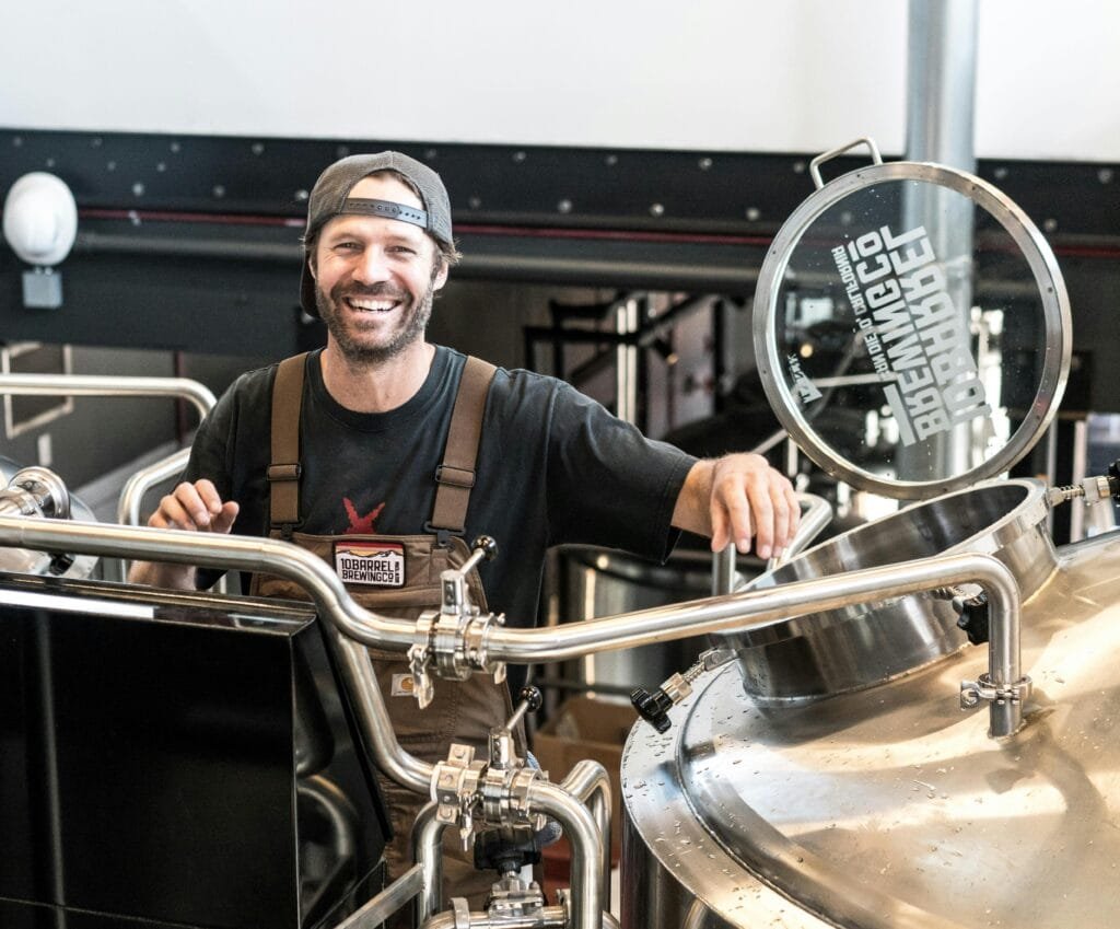 Happy brewer in a craft brewery standing near stainless steel equipment.