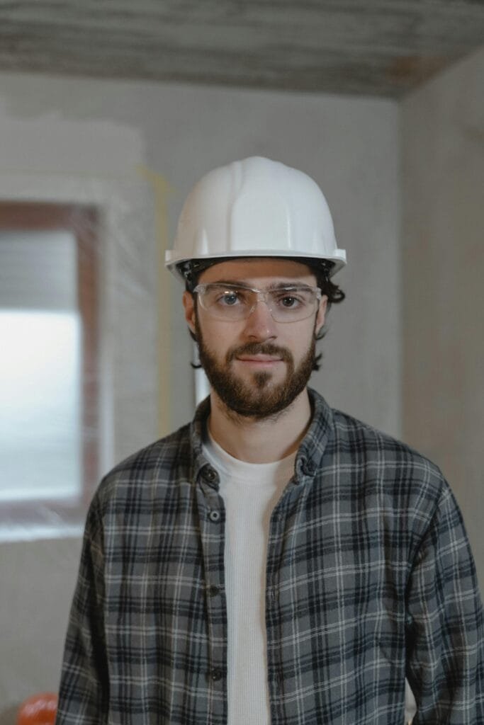 Portrait of a construction worker wearing a hard hat and safety glasses inside a building.